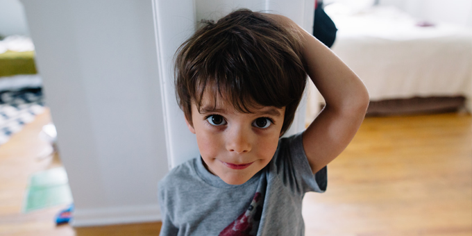 Young boy smiling with his hand on his head.