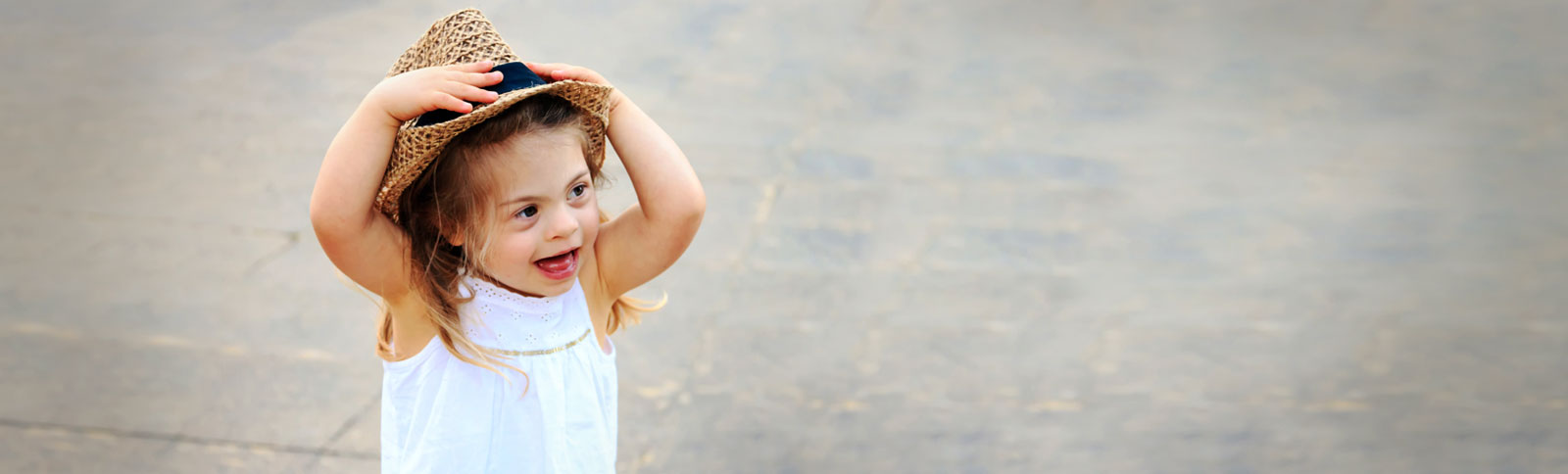 Happy, young girl with Down Syndrome, wearing a white Summery dress and grabbing her brown straw hat