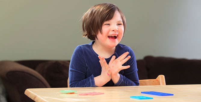 A joyful girl with down syndrome clapping her hands with a big smile.